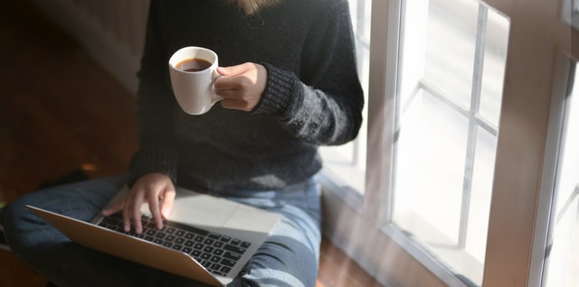 Žena s kávou v ruke píše na notebooku